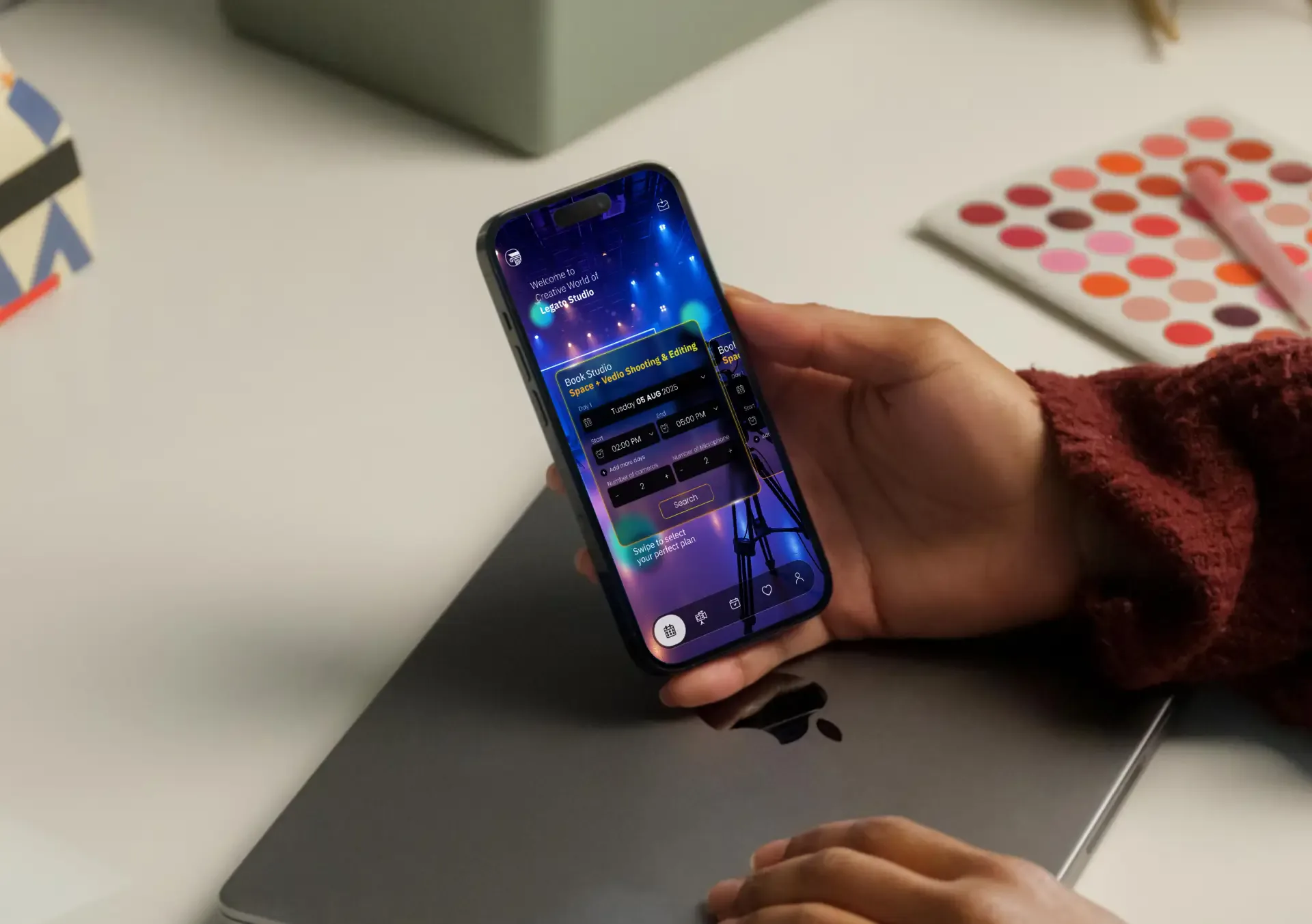 Hand holding a phone with the Legato Studio app above a laptop on a light desk