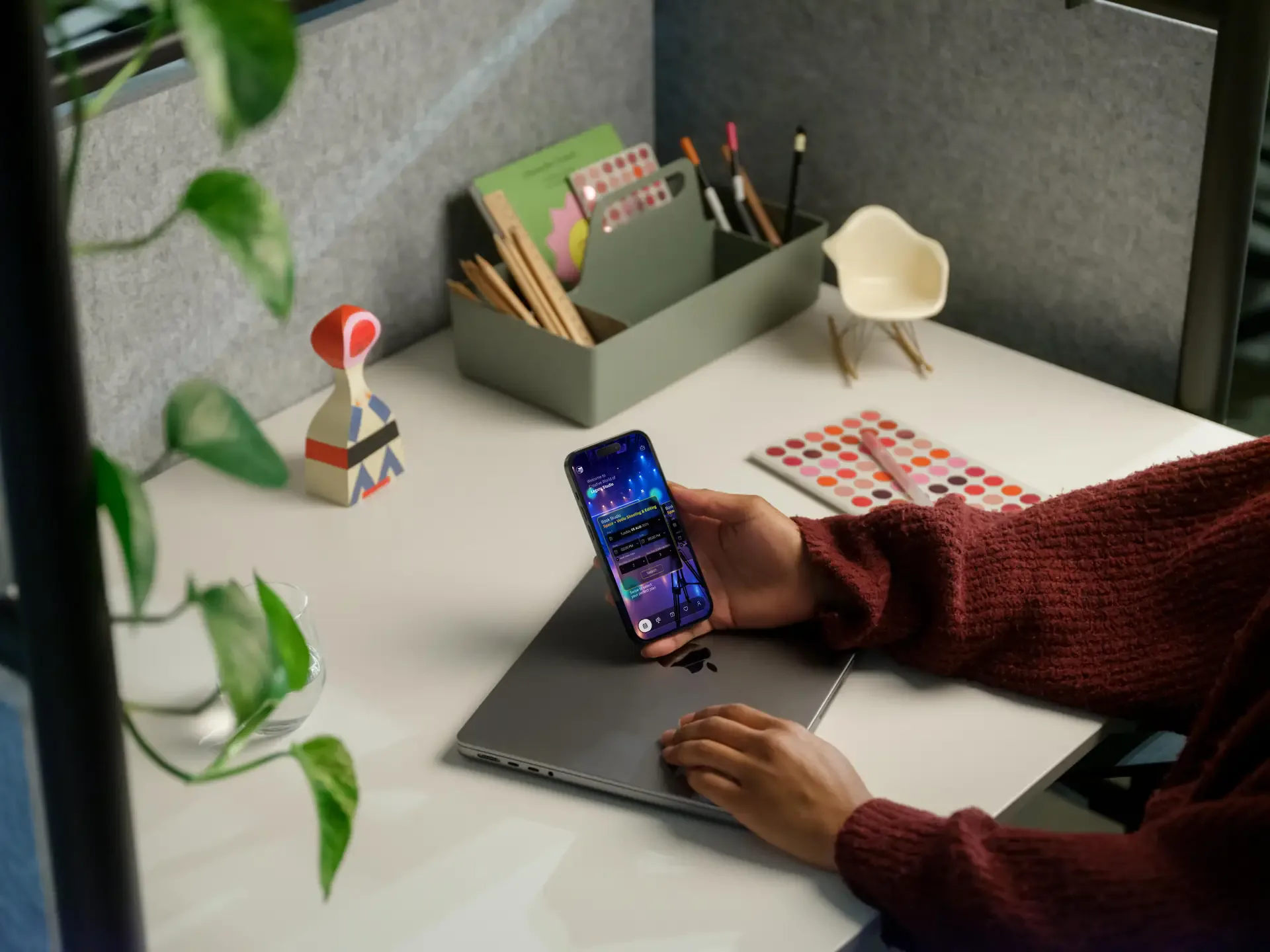 Person at a desk holding a phone with the Legato Studio app, plants and stationery around