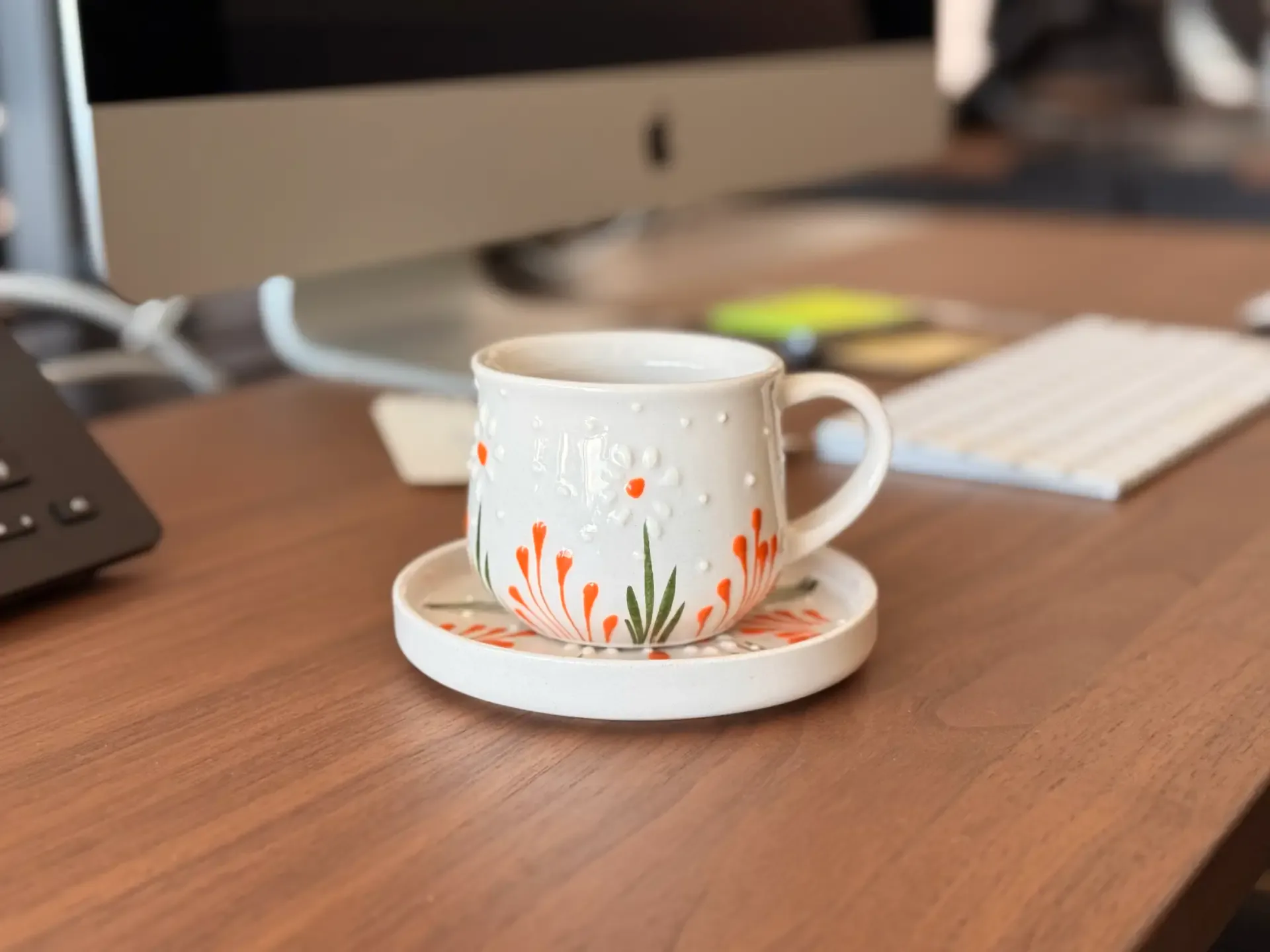 Floral coffee cup and saucer on a wooden desk beside a keyboard and monitor
