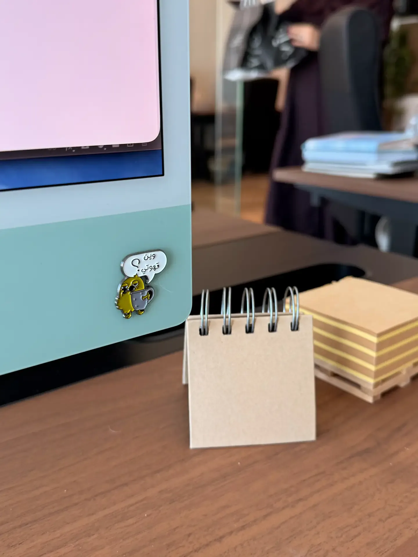 Spiral notepad and colour swatch cards on a wooden desk next to a monitor