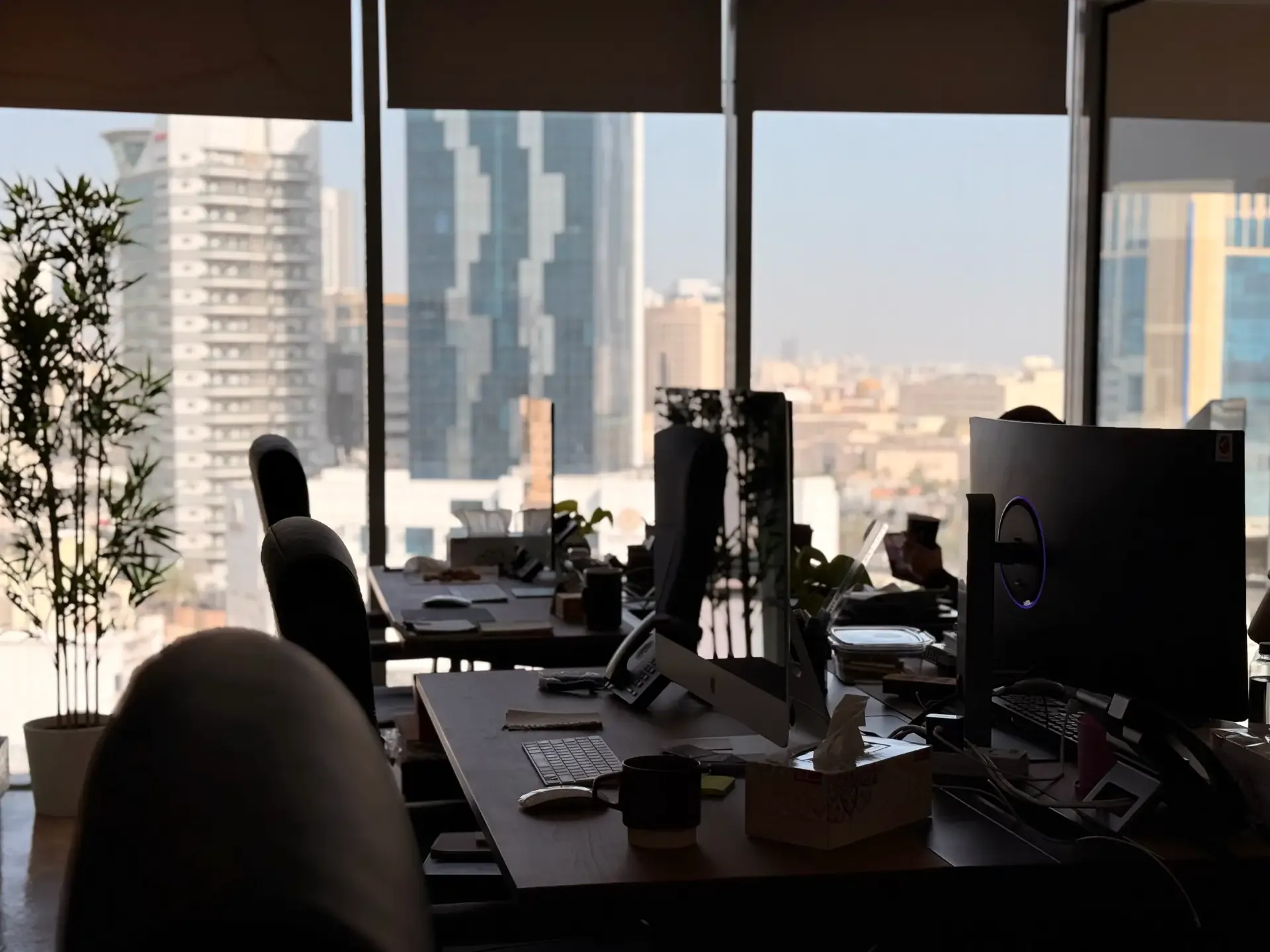 Open-plan Legato office with desks and monitors in front of floor-to-ceiling windows overlooking city towers