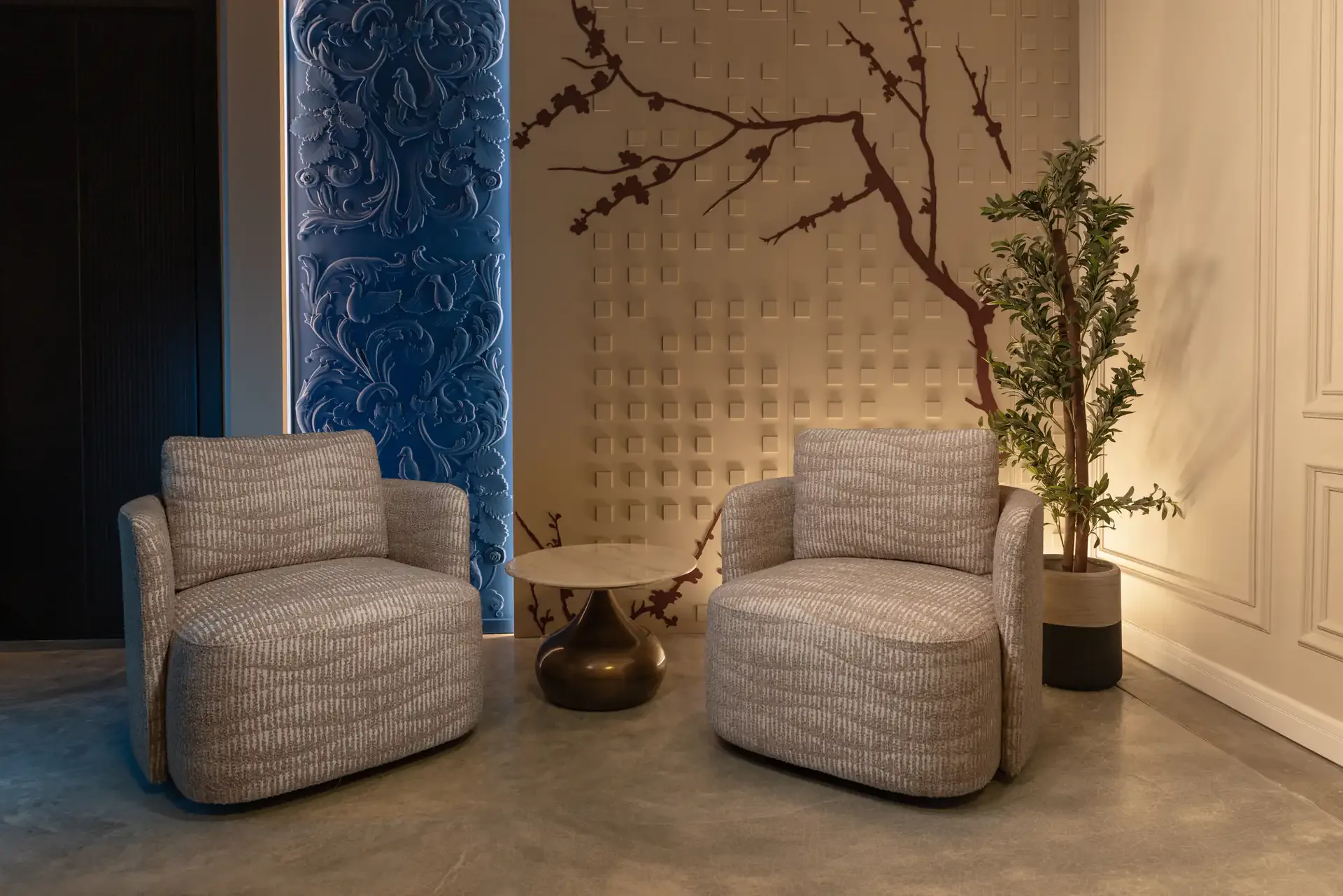 Bloom studio at Legato Studio: two textured armchairs before a blossom-branch wall and a carved blue panel