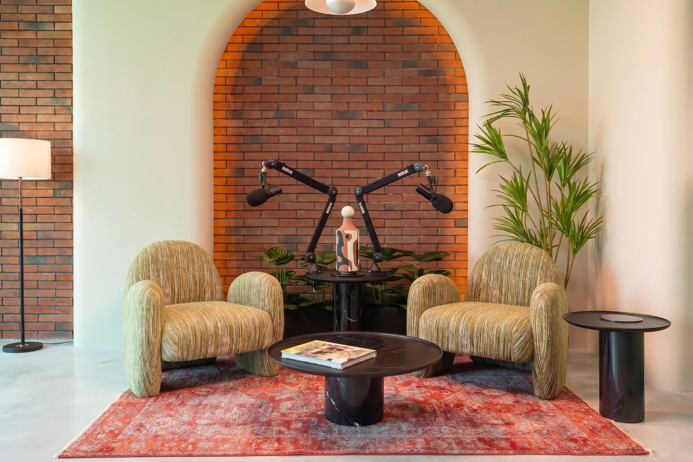 Eden studio at Legato Studio: striped armchairs and podcast mic arms under a red-brick arch on a red rug