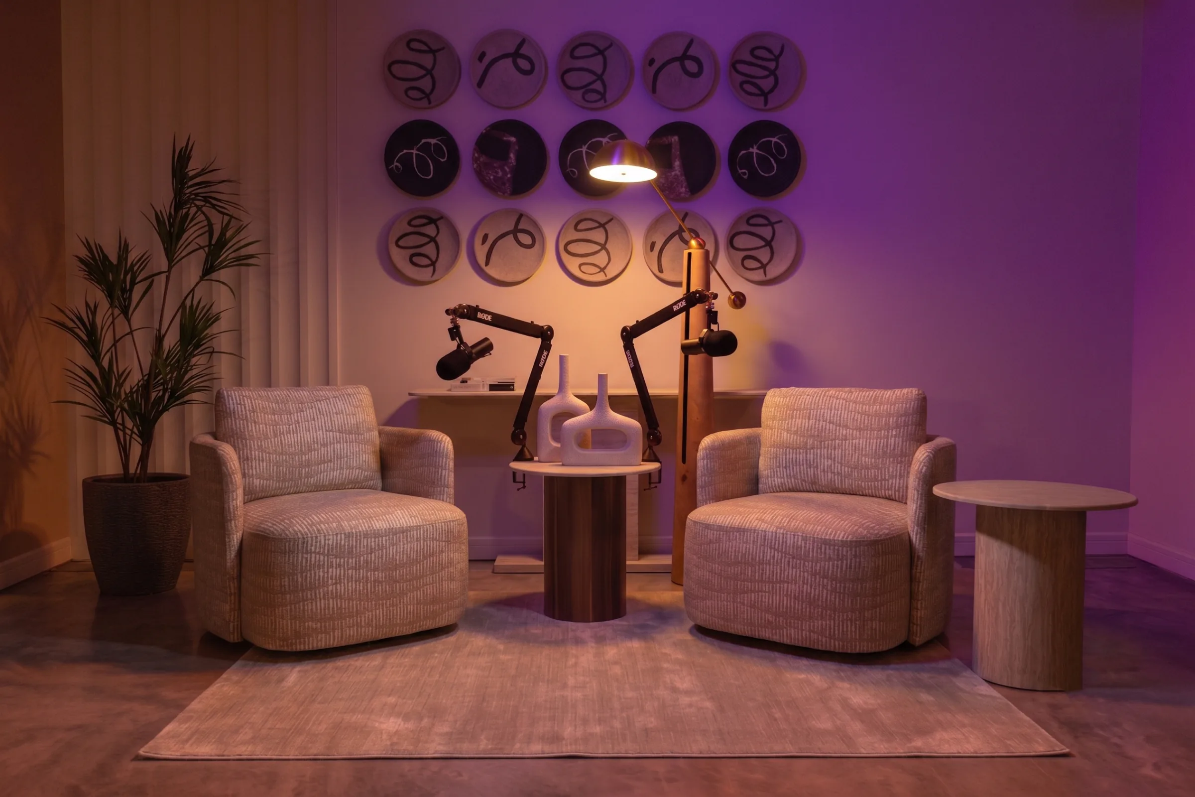 Loft studio at Legato Studio: two armchairs and podcast mic arms beneath decorative wall plates in warm and purple light