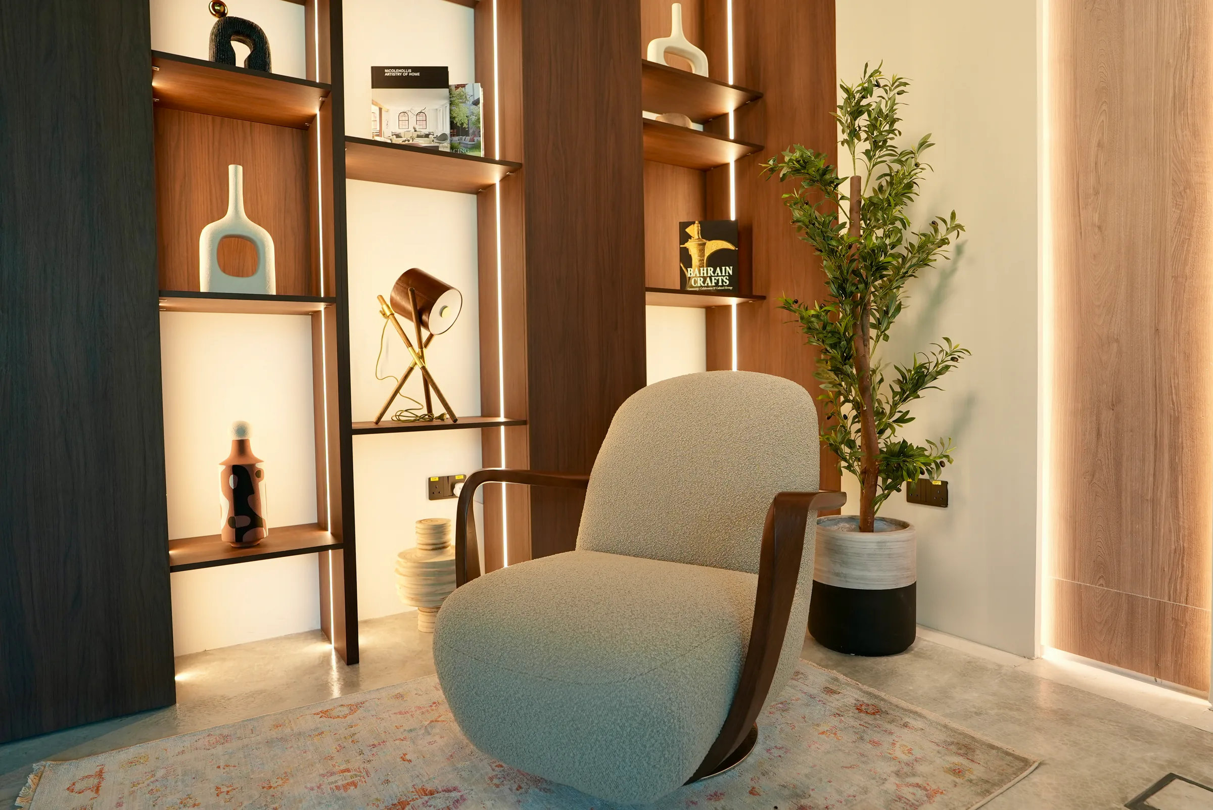 Nook studio at Legato Studio: a bouclé lounge chair beside backlit walnut bookshelves with vases and a desk lamp