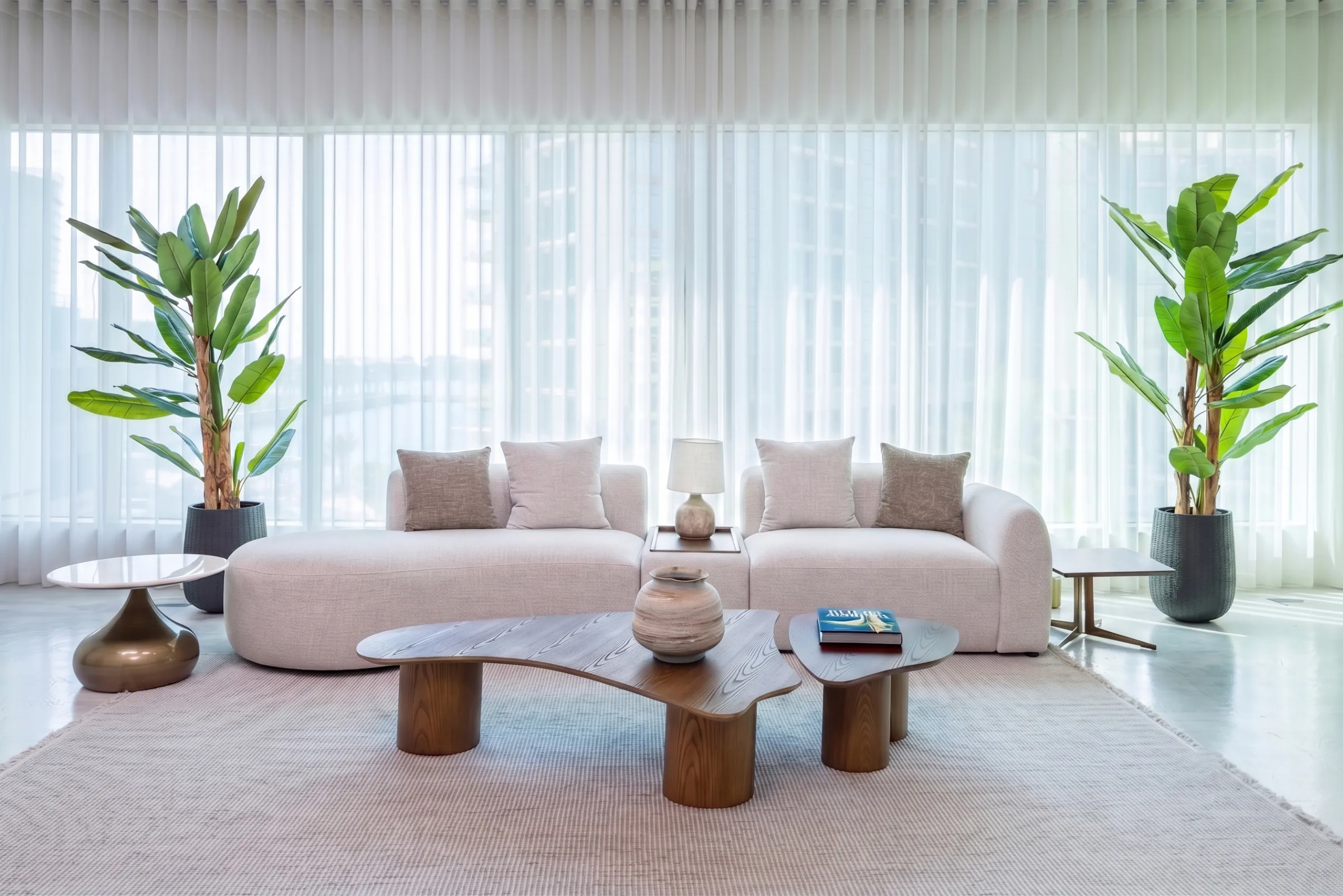 Nova studio at Legato Studio: cream sofa and sculpted walnut coffee tables before sheer curtains and city windows