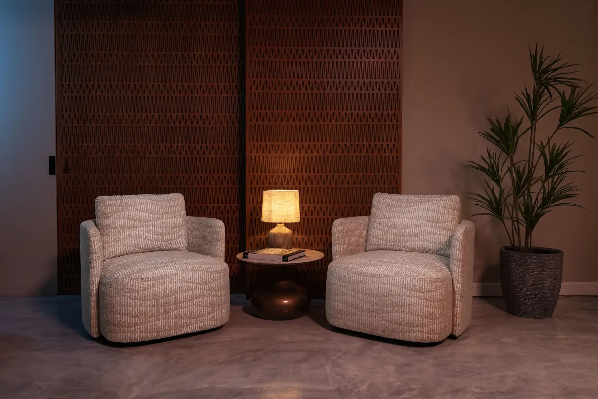 Woven studio at Legato Studio: two textured armchairs and a table lamp before a carved wooden lattice wall
