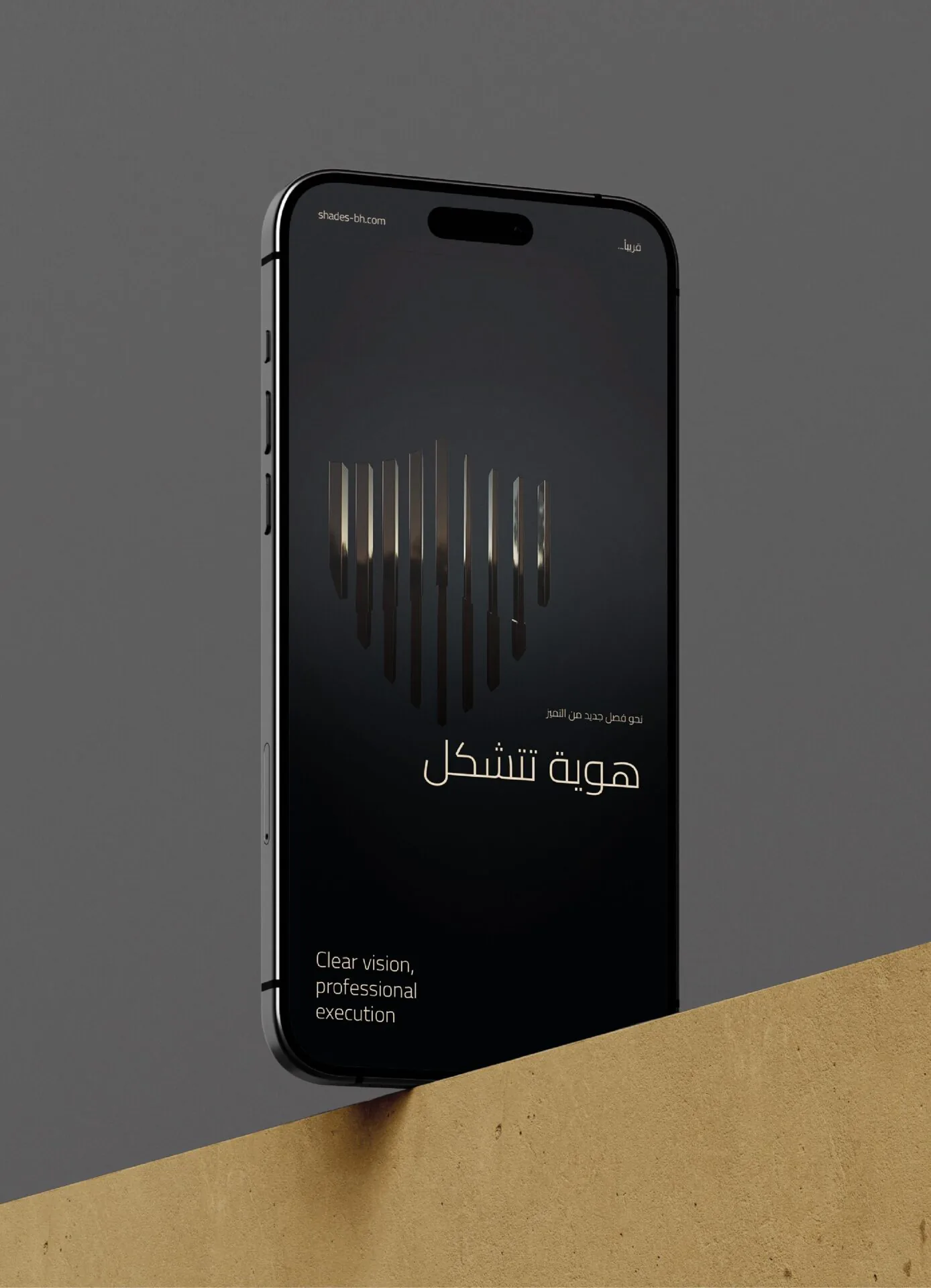 Black iPhone with the Shades Bailiff emblem and Arabic tagline, leaning on a sand block